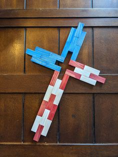 a wooden cross with red, white and blue strips painted on it sitting on a wood floor