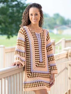 a woman standing on a bridge wearing a crocheted dress and smiling at the camera