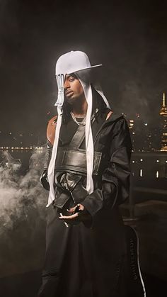 a man wearing a white hat and holding a knife in his hand while standing next to a city at night