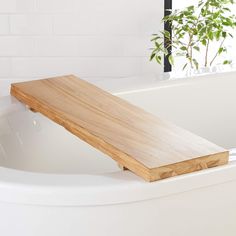 a wooden bench sitting on top of a white bath tub next to a potted plant