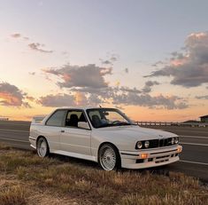 the white car is parked on the side of the road by the highway at sunset