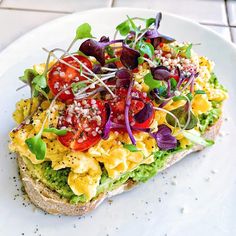 a white plate topped with a sandwich covered in veggies and toppings on top of it