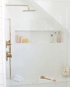 a bathroom with white tile and gold fixtures on the shower wall, along with toiletries