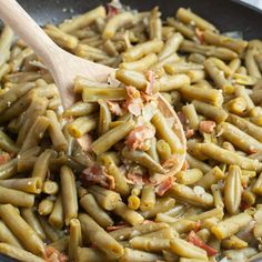 a pan filled with green beans covered in sauce and topped with a wooden spatula