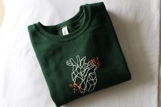 a green t - shirt with a cactus embroidered on the front sitting on a white sheet