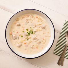 a bowl of chicken and dumpling soup next to a spoon on a white table