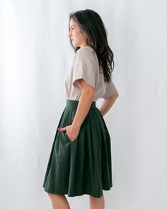 a woman standing in front of a white background wearing a green skirt and beige shirt