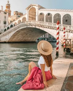 a woman in a hat sitting on the edge of a pier next to a bridge