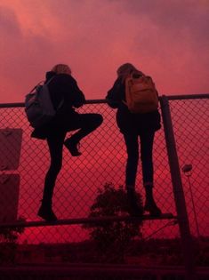 two girls standing on a fence with their backs to each other and the sky in the background