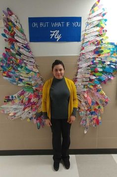 a woman standing in front of a wall covered in plastic bottles and paper angel wings