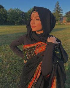 a woman in a black dress standing on top of a grass covered field with her hands on her hips