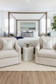 a white bedroom with four poster bed and two chairs