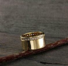 two gold wedding rings sitting on top of a piece of wood next to a pencil