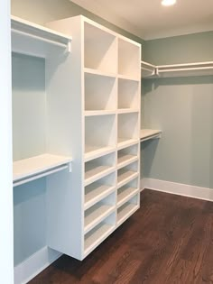 an empty walk in closet with white shelving and wood flooring on the side