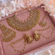 a pink tray with some gold jewelry on it and flowers in the backgroud