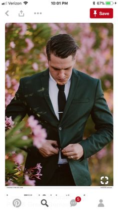 a man in a suit and tie standing next to pink flowers with his hands on his chest