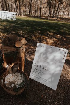 a sign and basket sitting on the ground in front of a forest with white chairs