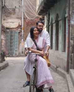 a man and woman riding on the back of a bicycle