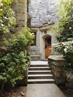 a stone house with steps leading up to the front door and entry way, surrounded by greenery