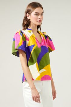 Introducing the whimsical wonder of the Rio Abstract Split Neck Poplin Top– where comfort meets color in a playful dance of poplin cotton perfection! Adorned with small ruffle ends on the shoulders and around the neckline plus a smooth outlined deep v-cut frame. So, go ahead, seize the day, and let your vibrant spirit shine through!- Ruffle detail- Split neckline- Short sleeves- Relaxed fit- Color: Khaki MultiSize + Fit - Model is 5'8" and wearing size XS- Measurements taken from size S - Chest: Playful Summer Blouse With Ruffles, Playful Ruffled Blouse For Summer, Vibrant Cotton Tops For Spring, Playful Ruffled Blouse For Spring, Vibrant Cotton Floral Print Top, Vibrant Floral Print Cotton Tops, Spring Multicolor Cotton Blouse, Multicolor Cotton Blouse For Spring, Vibrant Cotton Summer Tops