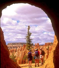 two people are standing in a cave looking at the view from inside it, with clouds overhead