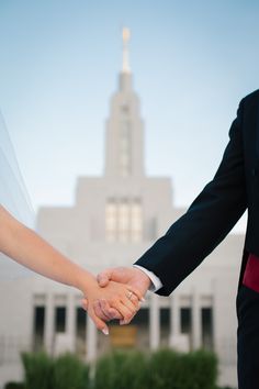 a bride and groom holding hands in front of a building with a spire on top