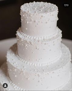 a three tiered white wedding cake with pearls on it