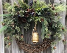 a wreath hanging on the side of a wooden fence with a bell and evergreens