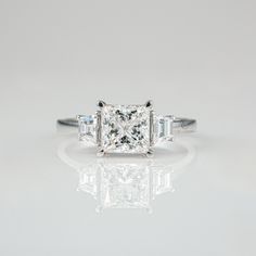 a princess cut diamond ring with three baguets on the sides and side stones