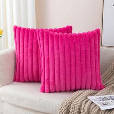 two pink pillows sitting on top of a white couch next to a vase with yellow flowers