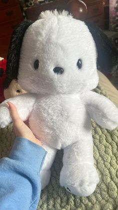 a white teddy bear sitting on top of a bed next to a child's hand