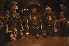 three men in pirate costumes stand at a table with other people standing around the table