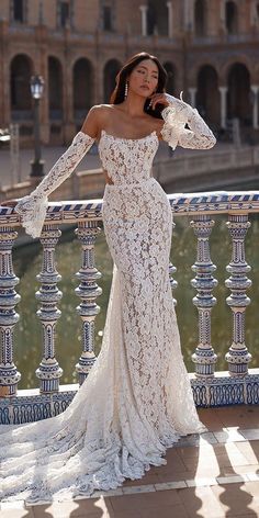 a woman in a white lace dress standing on a balcony next to a fountain and looking off into the distance