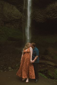 a man and woman standing in front of a waterfall