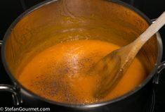 a wooden spoon in a pot filled with orange liquid on top of a black stove