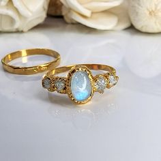 two yellow gold rings with blue and white stones on the sides, one is in front of flowers