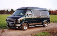 a black van parked on top of a dirt road next to a lush green field