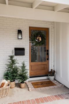 the front door is decorated with wreaths and potted trees for holiday decorating