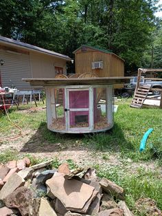 a chicken coop in the middle of a yard with rocks and grass around it,