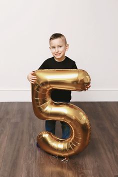 a young boy is holding an inflatable number 5 balloon