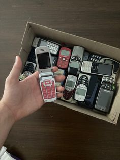 a person holding a cell phone in a box with many other phones inside it on a table