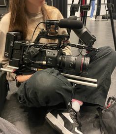 a woman is sitting on the floor with a camera in front of her and she is holding a video camera