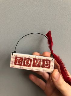 a hand holding a small wooden sign with the word love spelled in red on it