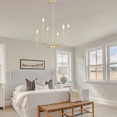 a bedroom with white furniture and large windows in it's centerpiece, along with a chandelier that hangs from the ceiling