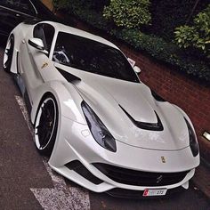 a white sports car parked on the side of the road next to a black car