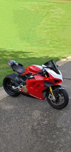 a red and white motorcycle parked on the side of a road next to a lush green field