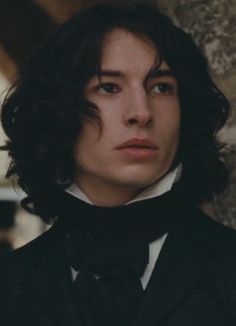 a man with long hair wearing a suit and bow tie looking off into the distance