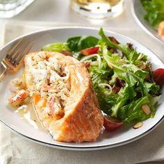 a white plate topped with salmon and salad next to a fork on a table cloth