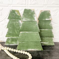 a green wooden christmas tree sitting on top of a table next to a beaded necklace