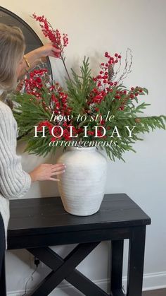 a woman arranging flowers in a white vase on a table with the words how to style holiday arrangements